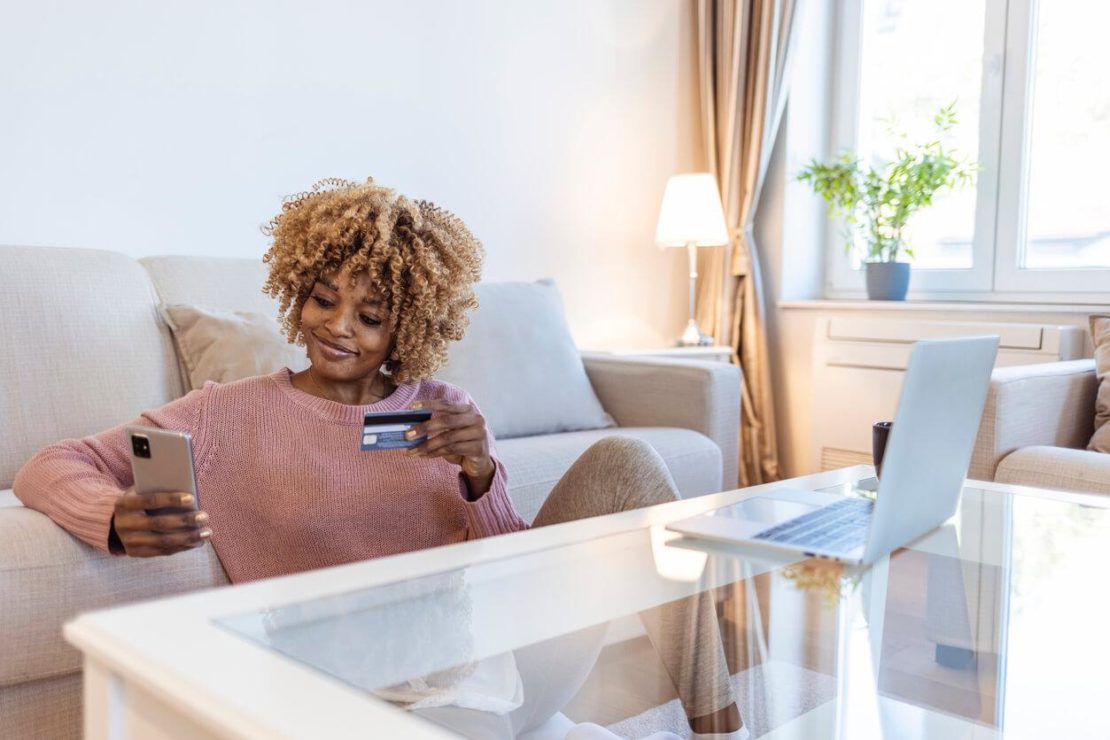 a women looking at her phone with a credit card in her hand, researching the answer to "what is a contact center?"