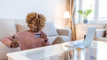 a women looking at her phone with a credit card in her hand, researching the answer to "what is a contact center?"