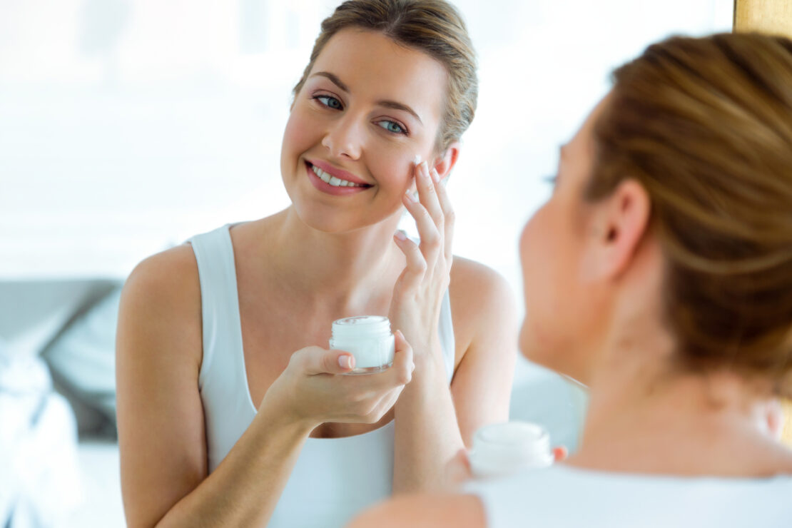 Portrait of beautiful young woman caring of her skin standing near mirror in the bathroom.