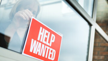 a person hanging a Help Wanted sign in response to the US Labor Shortage