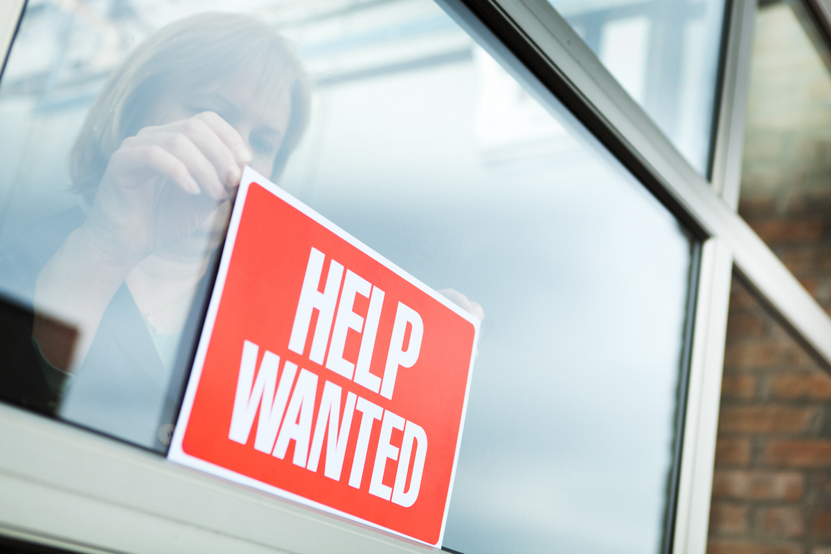 a person hanging a Help Wanted sign in response to the US Labor Shortage