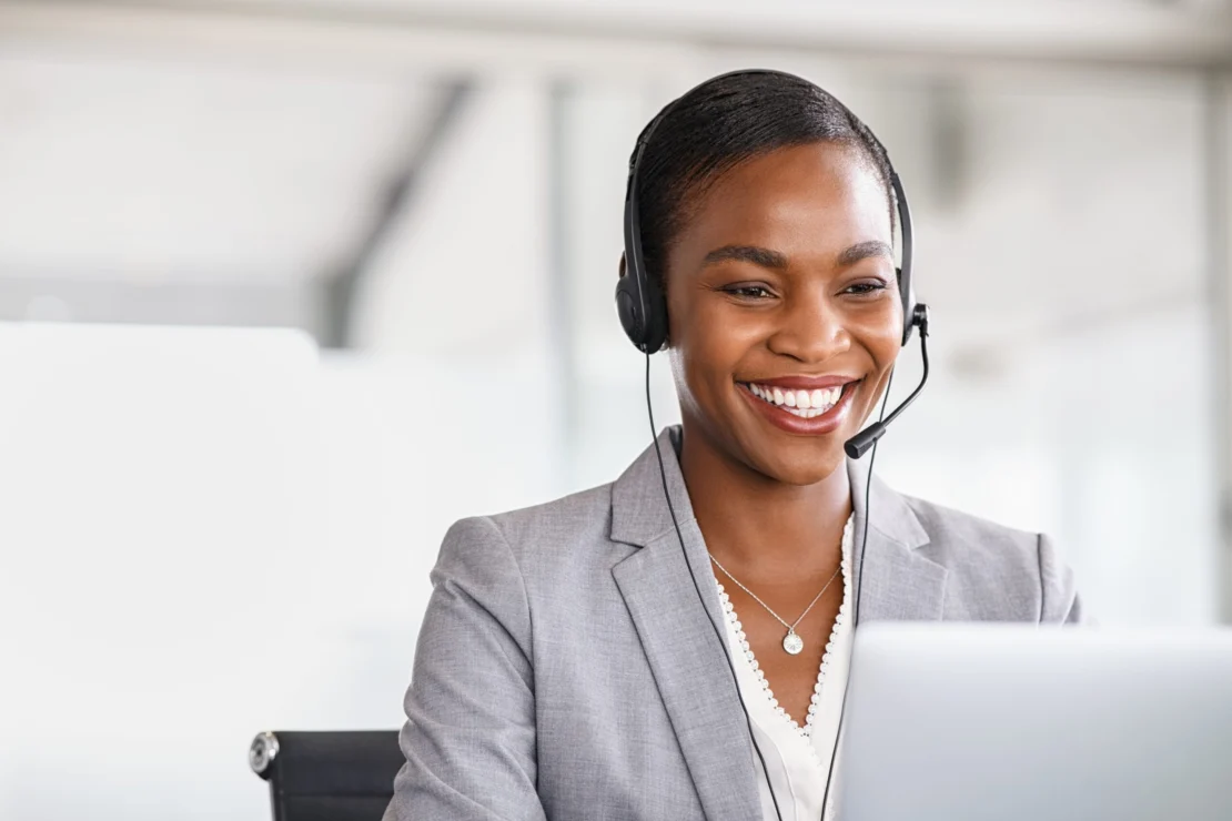 A smiling customer service agent wearing a headset and using a computer.
