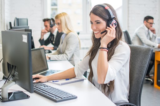 Happy female call center agent speaking on a headset while sitting at her computer