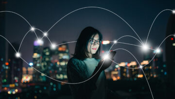 A woman looks at her smartphone and smiles, with a city skyline in the background and a connected network of lights superimposed on top.