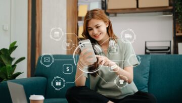 A customer sits on her couch and smiles at her phone, with a web of communication channels emerging from the phone.