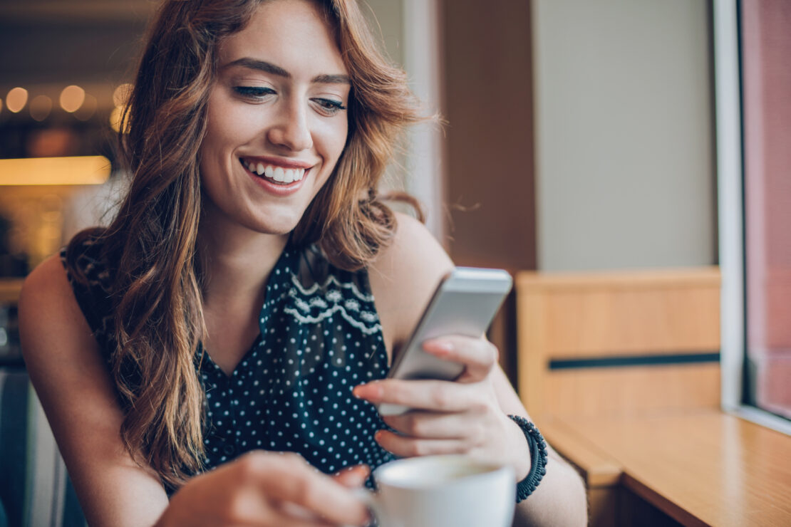 A woman smiles, while checking her phone, pleased at her customer experience.