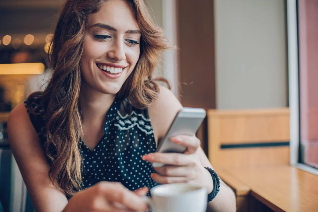 A woman smiles, while checking her phone, pleased at her customer experience.