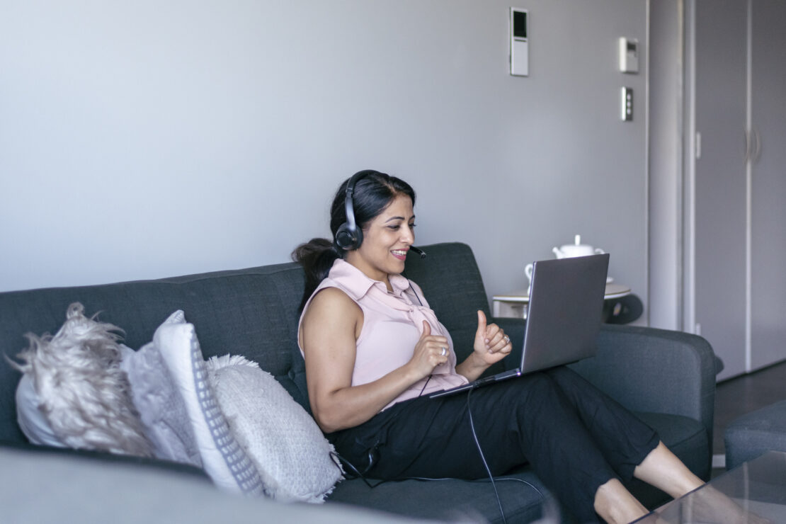 A call center agent takes a call using her laptop while sitting in her home living room.