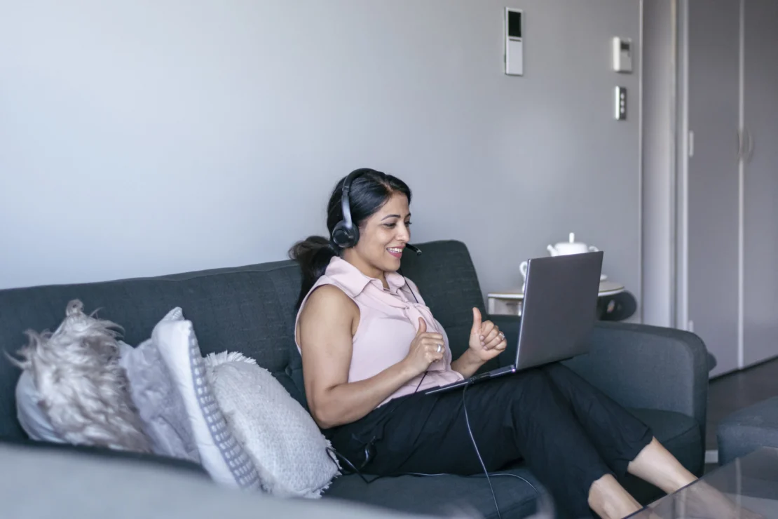 A call center agent takes a call using her laptop while sitting in her home living room.