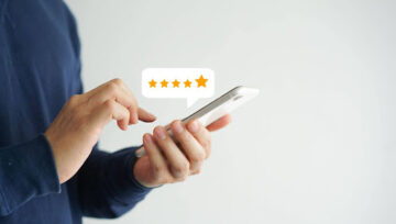 Hands hold a phone, poised to give a five-star review depicted by a chat bubble with five stars filled out.