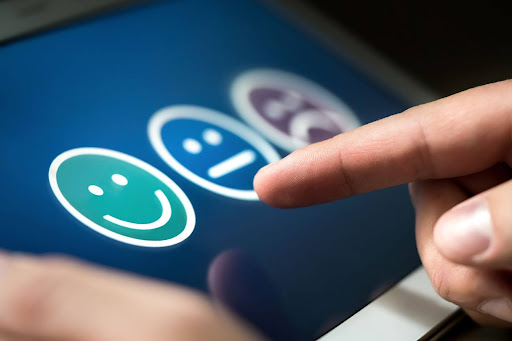 A customer fills out a satisfaction survey with a finger poised to select the smiley face option.
