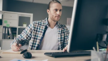 Young bearded man on his computer writing down notes
