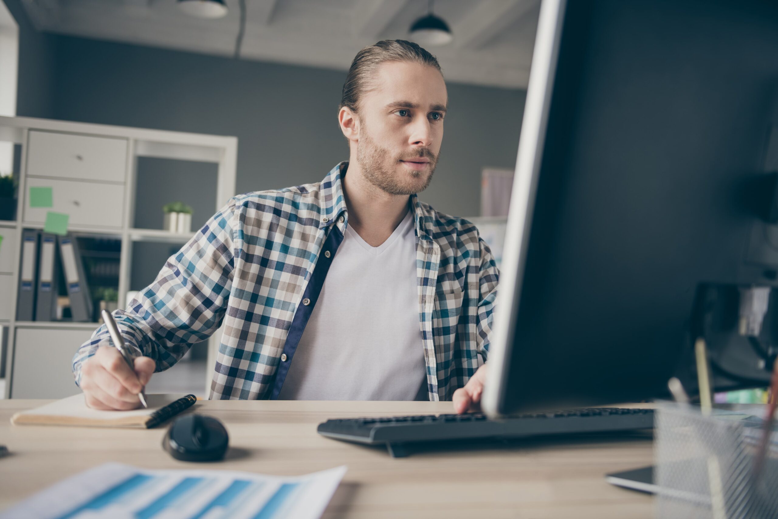 Young bearded man on his computer writing down notes