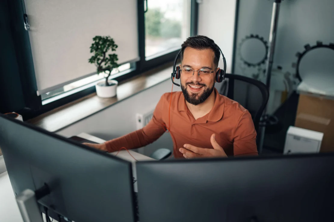 telemarketing agent smiling talking on his headset in front of his computer