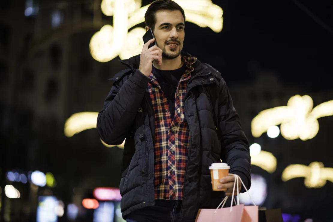 man on his cell phone holding a shopping bag and coffee at night